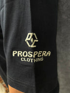 Close-up of a black garment sleeve with a gold embroidered logo and the text PROSPERA CLOTHING